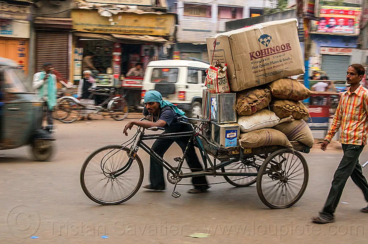 man pushing cargo tricycle with heavy load, india