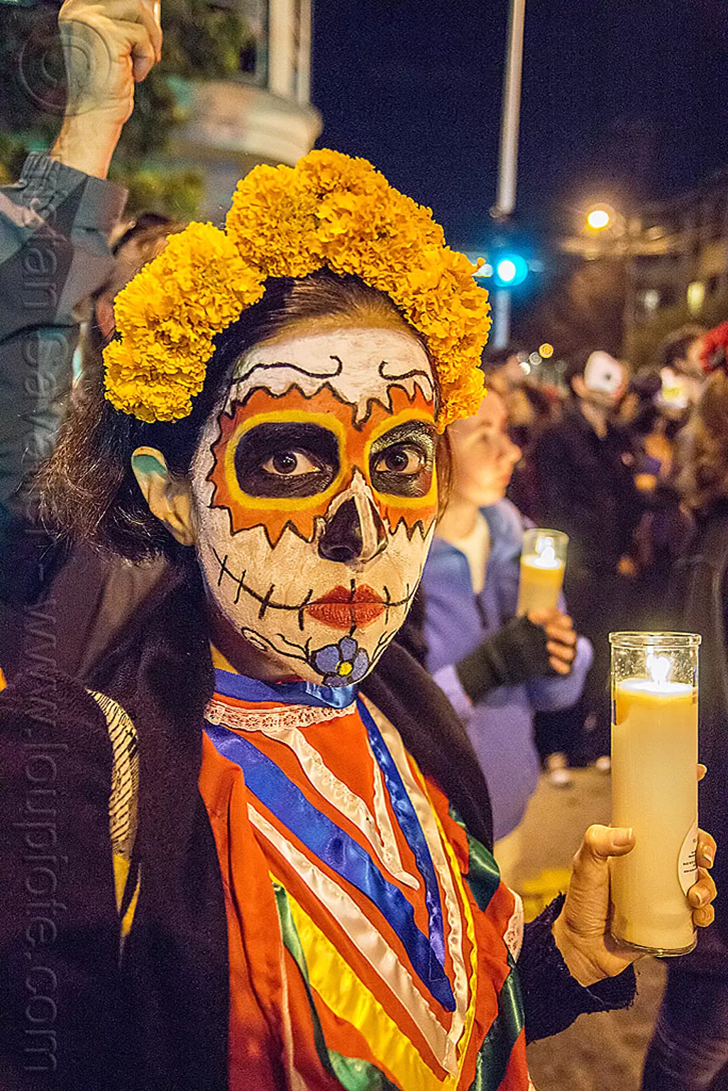 woman with skull makeup, marigold flower headdress, holding glass