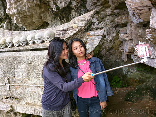 local girls taking a selfie with ancient coffin and human skulls - ke'te kesu' traditional toraja burial site, cemetery, erong coffin, girls, grave, graveyard, human bones, human skulls, kete kesu burial site, liang, selfie, tana toraja, tomb, women