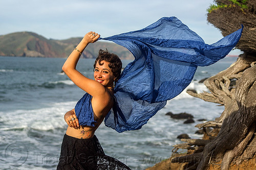 woman holding blue scarf in the wind on ocean shore